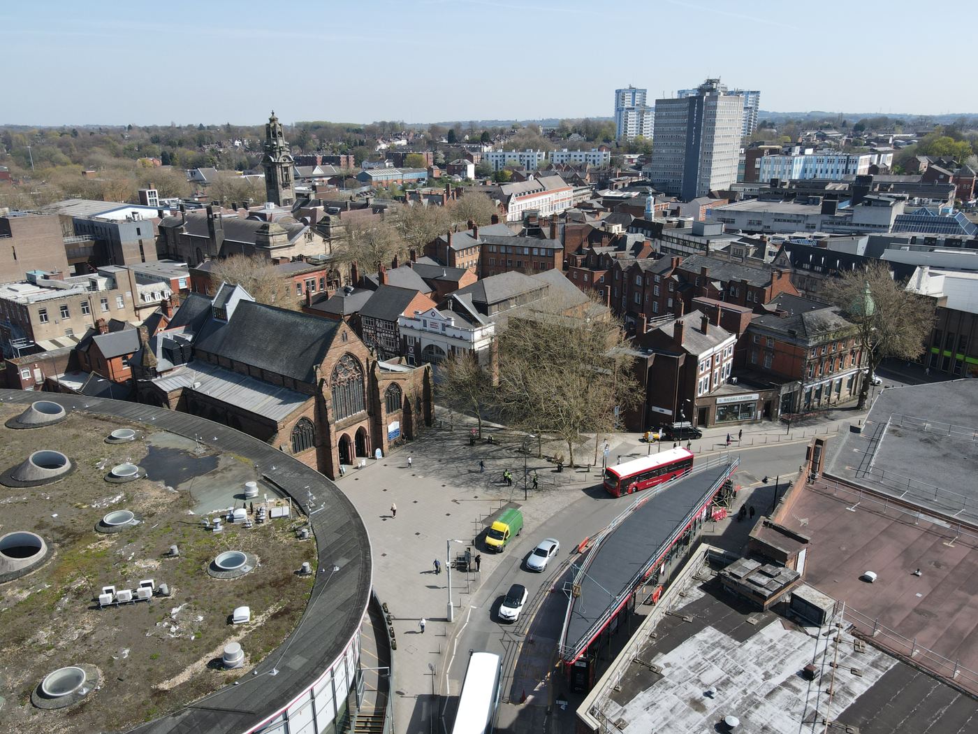 Walsall town centre from above: the bus station roof in the foreground, the red sandstone church of St Paul behind it, shops, trees, and tower blocks in the distance.